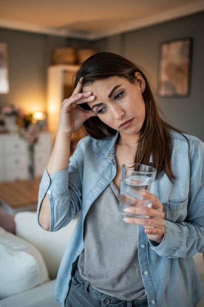 Woman holding water glass preparing to take Audifort hearing supplement